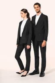 Jeune homme aux cheveux châtains courts et jeune femme aux cheveux châtains longs attachés en queue de cheval composent un duo élégant en noir et blanc. Ils portent chacun une veste noire à la coupe ajustée, associée à une chemise blanche, un pantalon noi