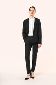 Jeune femme aux cheveux châtains longs attachés en queue de cheval portant une veste blazer noire à la coupe ajustée, confectionnée dans un mélange de matières de qualité (50% polyester, 23% viscose, 22% laine, 5% élasthanne) offrant confort et chaleur. L