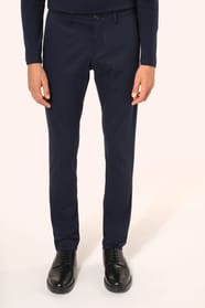 Jeune homme aux cheveux châtains courts portant un chino bleu profond à la coupe straight, moderne et tendance. Confectionné en coton et élasthanne, il associe confort, souplesse et résistance, idéal en toutes saisons. Il l’associe à un T-shirt col V bleu