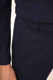 Jeune homme aux cheveux châtains courts portant un chino bleu profond à la coupe straight, moderne et tendance. Confectionné en coton et élasthanne, il associe confort, souplesse et résistance, idéal en toutes saisons. Il l’associe à un T-shirt col V bleu