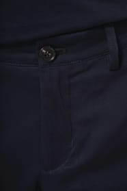 Jeune homme aux cheveux châtains courts portant un chino bleu profond à la coupe straight, moderne et tendance. Confectionné en coton et élasthanne, il associe confort, souplesse et résistance, idéal en toutes saisons. Il l’associe à un T-shirt col V bleu