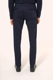 Jeune homme aux cheveux châtains courts portant un chino bleu profond à la coupe straight, moderne et tendance. Confectionné en coton et élasthanne, il associe confort, souplesse et résistance, idéal en toutes saisons. Il l’associe à un T-shirt col V bleu