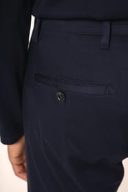 Jeune homme aux cheveux châtains courts portant un chino bleu profond à la coupe straight, moderne et tendance. Confectionné en coton et élasthanne, il associe confort, souplesse et résistance, idéal en toutes saisons. Il l’associe à un T-shirt col V bleu