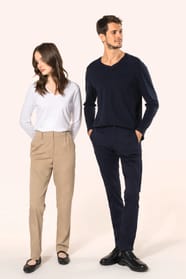 Jeune homme aux cheveux châtains courts et jeune femme aux cheveux châtains longs, détachés et légèrement ondulés, composent un duo élégant et moderne. Il porte un chino bleu profond à la coupe straight, associé à un T-shirt col V bleu assorti, alliant co