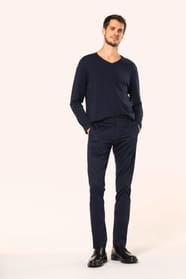 Jeune homme aux cheveux châtains courts portant un chino bleu profond à la coupe straight, moderne et tendance. Confectionné en coton et élasthanne, il associe confort, souplesse et résistance, idéal en toutes saisons. Il l’associe à un T-shirt col V bleu
