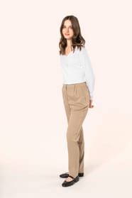 Jeune femme aux cheveux châtains longs, détachés et légèrement ondulés, portant un pantalon sable en tissu twill, élégant et confortable, composé de viscose, associé à une chemise blanche intemporelle. Cet ensemble sobre et raffiné allie modernité et conf