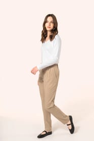 Jeune femme aux cheveux châtains longs, détachés et légèrement ondulés, portant un pantalon sable en tissu twill, élégant et confortable, composé de viscose, associé à une chemise blanche intemporelle. Cet ensemble sobre et raffiné allie modernité et conf