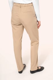 Jeune femme portant un pantalon sable en tissu twill, élégant et confortable, composé de viscose, associé à une chemise blanche intemporelle. Cet ensemble sobre et raffiné allie modernité et confort au quotidien.