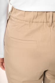 Jeune femme portant un pantalon sable en tissu twill, élégant et confortable, composé de viscose, associé à une chemise blanche intemporelle. Cet ensemble sobre et raffiné allie modernité et confort au quotidien.