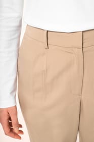 Jeune femme portant un pantalon sable en tissu twill, élégant et confortable, composé de viscose, associé à une chemise blanche intemporelle. Cet ensemble sobre et raffiné allie modernité et confort au quotidien.