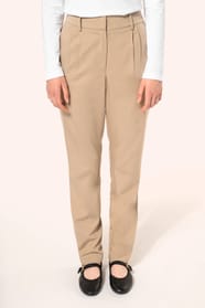 Jeune femme portant un pantalon sable en tissu twill, élégant et confortable, composé de viscose, associé à une chemise blanche intemporelle. Cet ensemble sobre et raffiné allie modernité et confort au quotidien.