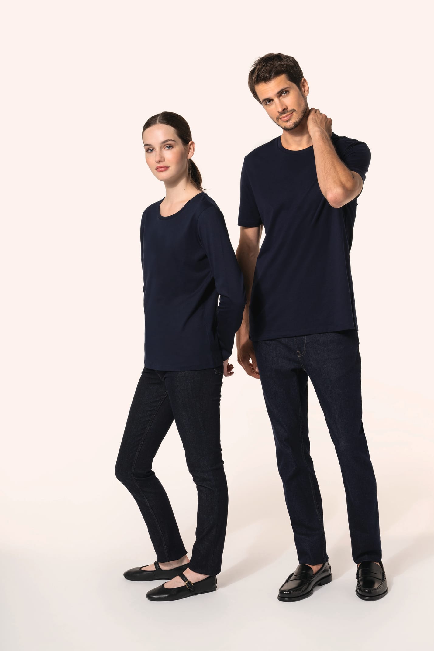 Jeune homme aux cheveux châtains courts et jeune femme aux cheveux châtains longs attachés portent chacun un jean ajusté en denim (99% coton, 1% élasthanne) à la coupe straight, confortable et moderne. Leurs finitions soignées incluent une mercerie et des