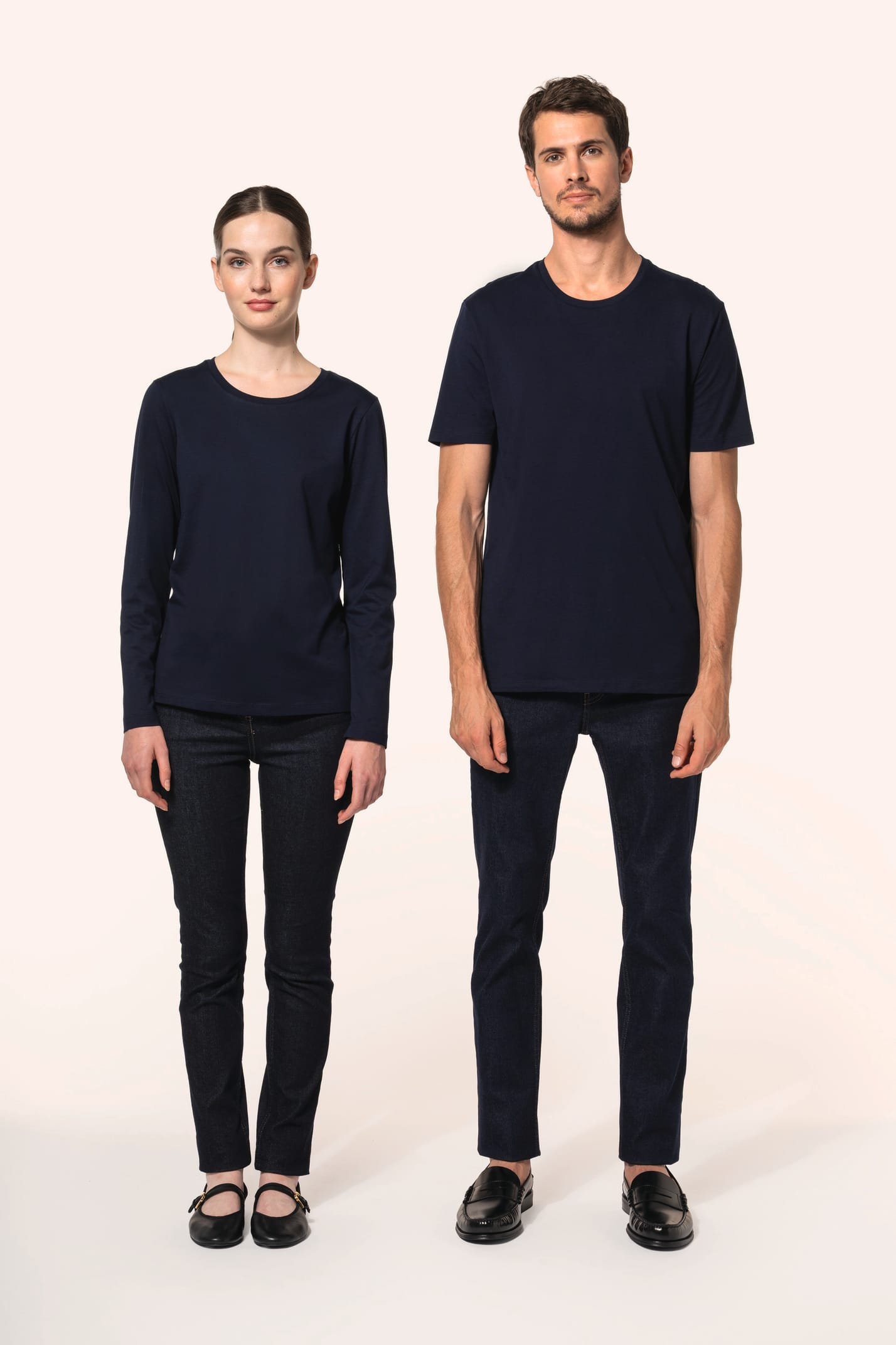 Jeune homme aux cheveux châtains courts et jeune femme aux cheveux châtains longs attachés portent chacun un jean ajusté en denim (99% coton, 1% élasthanne) à la coupe straight, confortable et moderne. Leurs finitions soignées incluent une mercerie et des