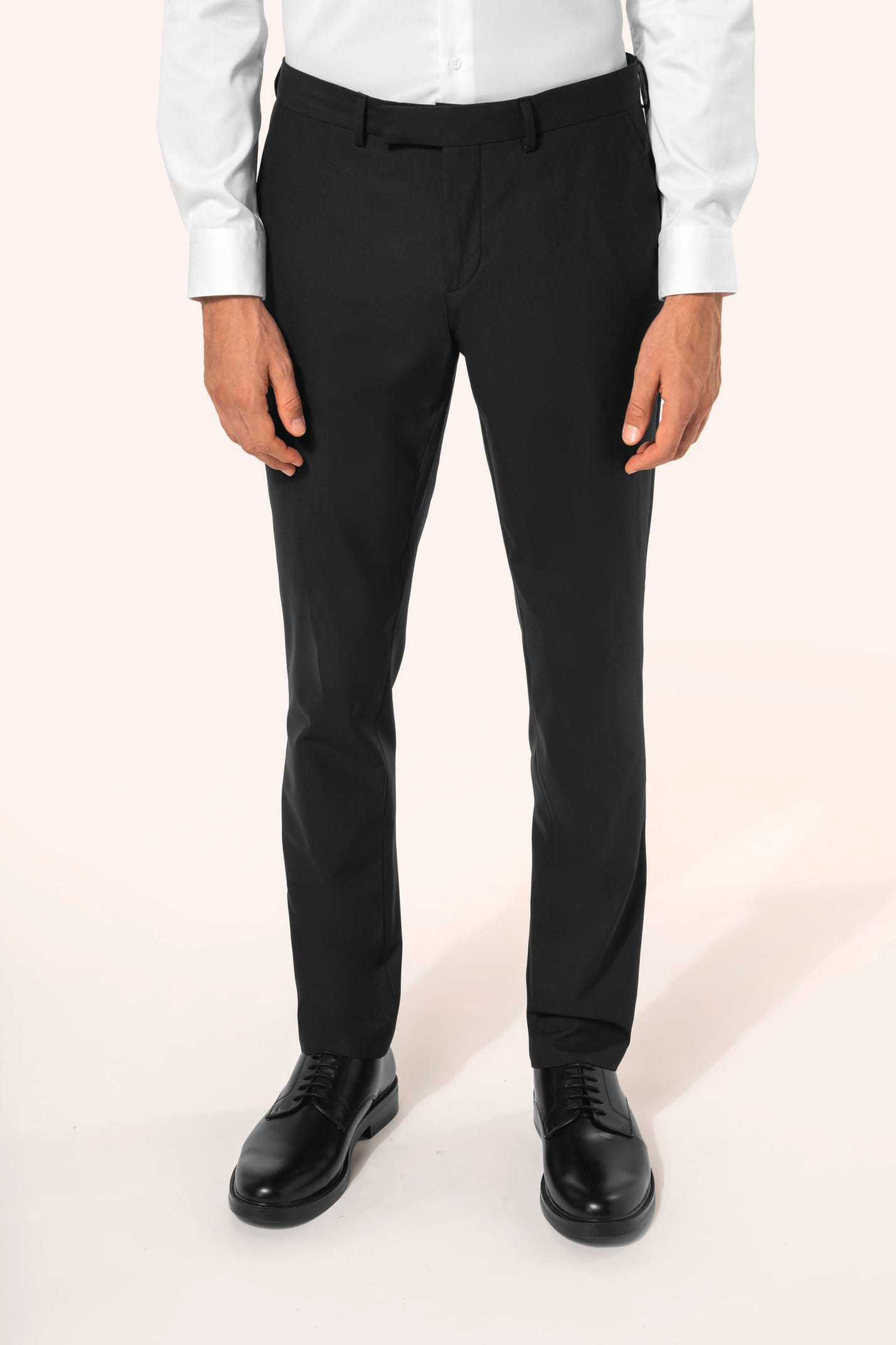 Homme portant un pantalon de costume noir à la coupe straight élégante, associé à une chemise blanche rentrée et une ceinture assortie. L’ensemble est complété par des chaussures de ville en cuir noir brillant, pour une silhouette sobre et sophistiquée.