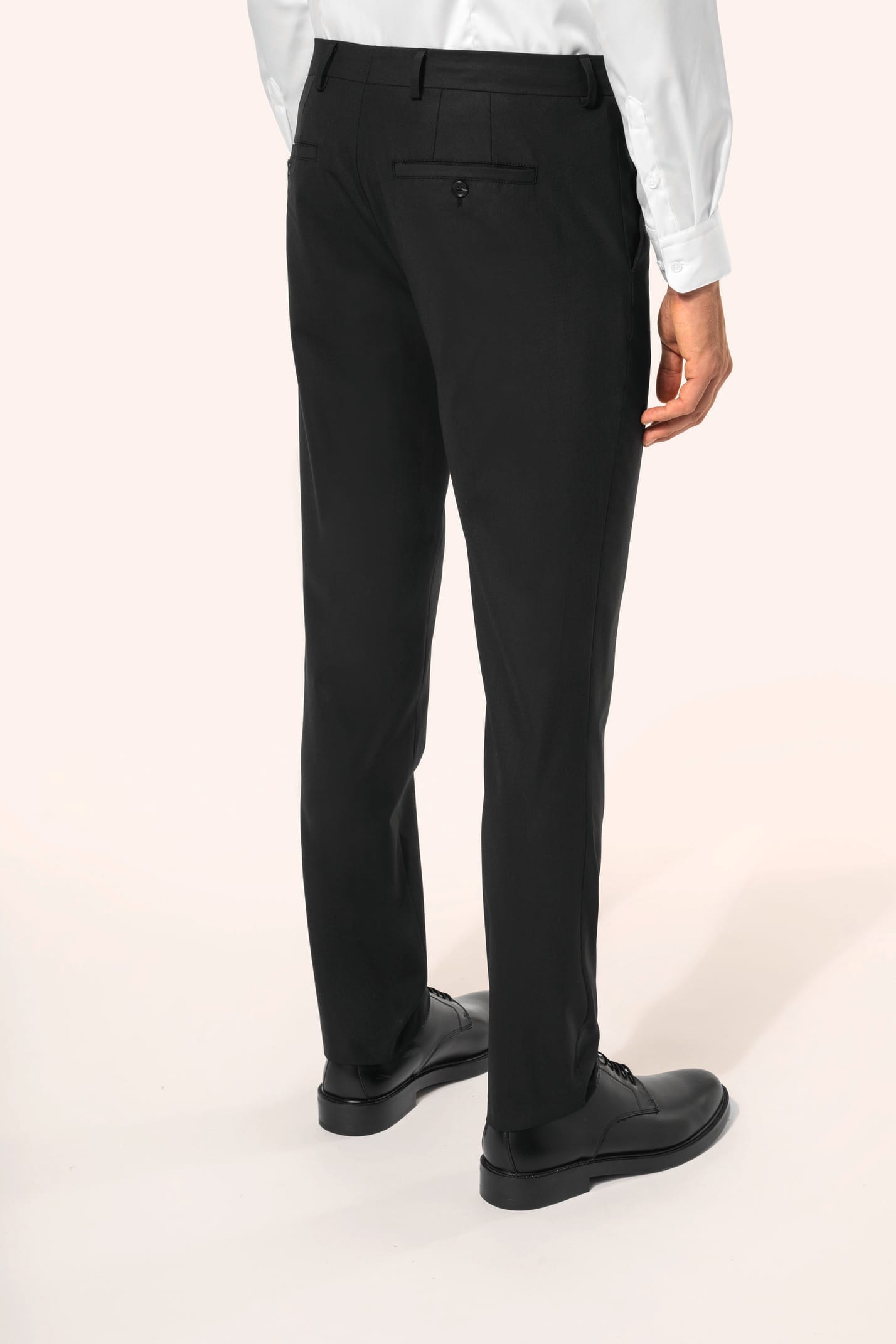 Homme portant un pantalon de costume noir à la coupe straight élégante, associé à une chemise blanche rentrée et une ceinture assortie. L’ensemble est complété par des chaussures de ville en cuir noir brillant, pour une silhouette sobre et sophistiquée.