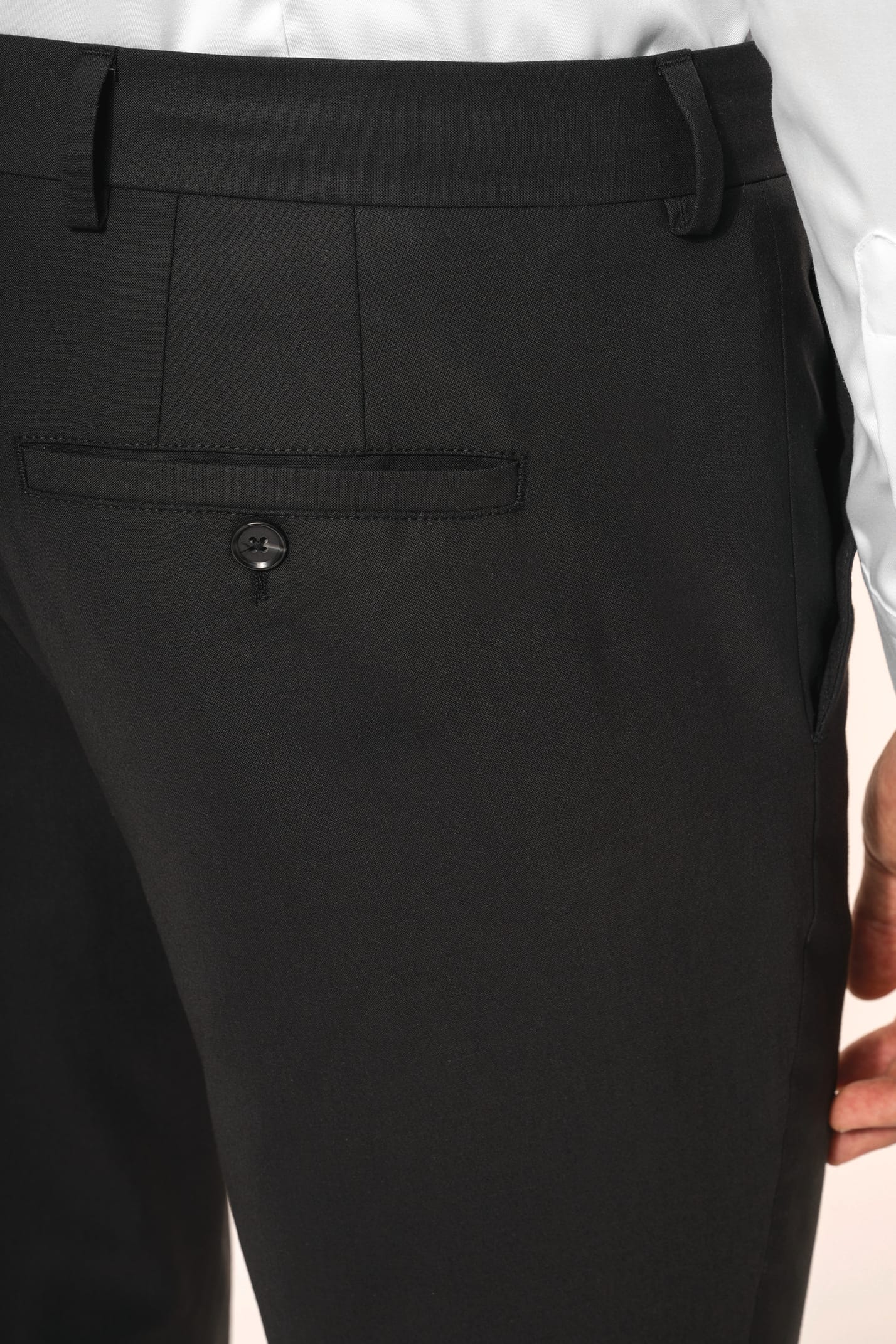 Homme portant un pantalon de costume noir à la coupe straight élégante, associé à une chemise blanche rentrée et une ceinture assortie. L’ensemble est complété par des chaussures de ville en cuir noir brillant, pour une silhouette sobre et sophistiquée.