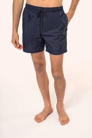 Jeune homme aux cheveux châtains courts et au physique athlétique, torse nu, portant un short de bain en tissu léger. Sa matière favorise un séchage rapide et intègre une poche arrière zippée, combinant confort et praticité pour un style sportif et modern