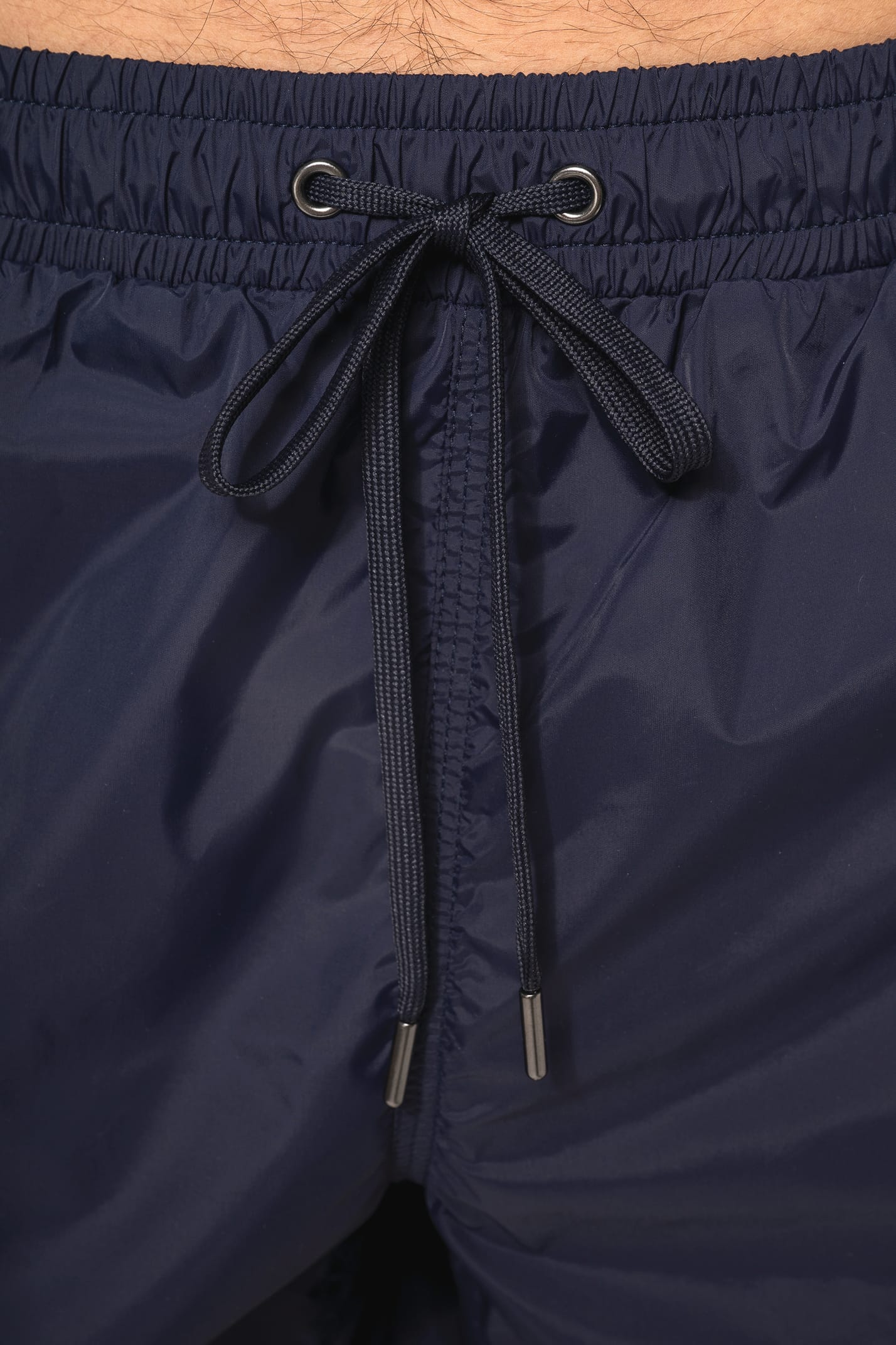 Jeune homme aux cheveux châtains courts et au physique athlétique, torse nu, portant un short de bain en tissu léger. Sa matière favorise un séchage rapide et intègre une poche arrière zippée, combinant confort et praticité pour un style sportif et modern