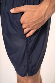 Jeune homme aux cheveux châtains courts et au physique athlétique, torse nu, portant un short de bain en tissu léger. Sa matière favorise un séchage rapide et intègre une poche arrière zippée, combinant confort et praticité pour un style sportif et modern