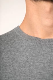 Jeune homme portant un pull gris clair chiné en coton Supima® col rond. Confectionné en fibres extra-longues, ce coton d’exception offre souplesse, douceur et durabilité. Sa maille révèle des points fantaisie obtenus par une technique de tricotage spécifi