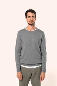 Jeune homme portant un pull gris clair chiné en coton Supima® col rond. Confectionné en fibres extra-longues, ce coton d’exception offre souplesse, douceur et durabilité. Sa maille révèle des points fantaisie obtenus par une technique de tricotage spécifi