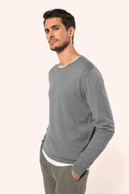 Jeune homme portant un pull gris clair chiné en coton Supima® col rond. Confectionné en fibres extra-longues, ce coton d’exception offre souplesse, douceur et durabilité. Sa maille révèle des points fantaisie obtenus par une technique de tricotage spécifi