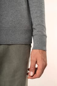 Jeune homme portant un pull gris clair chiné en coton Supima® col rond. Confectionné en fibres extra-longues, ce coton d’exception offre souplesse, douceur et durabilité. Sa maille révèle des points fantaisie obtenus par une technique de tricotage spécifi
