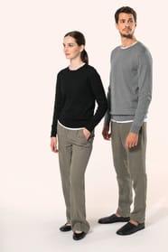 Jeune homme aux cheveux châtains courts et jeune femme aux cheveux châtains longs attachés en queue de cheval portent chacun un pull en coton Supima® col rond, reconnu pour la souplesse, la douceur et la durabilité de ses fibres extra-longues. Lui opte po