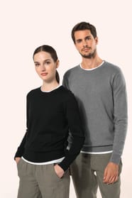 Jeune homme aux cheveux châtains courts et jeune femme aux cheveux châtains longs attachés en queue de cheval portent chacun un pull en coton Supima® col rond, reconnu pour la souplesse, la douceur et la durabilité de ses fibres extra-longues. Lui opte po