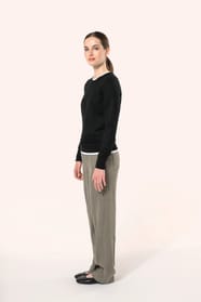 Jeune femme aux cheveux châtains longs attachés en queue de cheval portant un pull noir en coton Supima® col rond. Confectionné en fibres extra-longues, ce coton d’exception offre souplesse, douceur et durabilité. Sa maille révèle des points fantaisie obt
