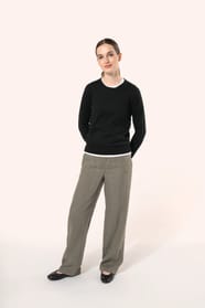 Jeune femme aux cheveux châtains longs attachés en queue de cheval portant un pull noir en coton Supima® col rond. Confectionné en fibres extra-longues, ce coton d’exception offre souplesse, douceur et durabilité. Sa maille révèle des points fantaisie obt