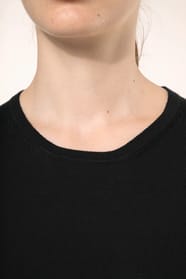 Jeune femme aux cheveux châtains longs attachés en queue de cheval portant un pull noir en coton Supima® col rond. Confectionné en fibres extra-longues, ce coton d’exception offre souplesse, douceur et durabilité. Sa maille révèle des points fantaisie obt
