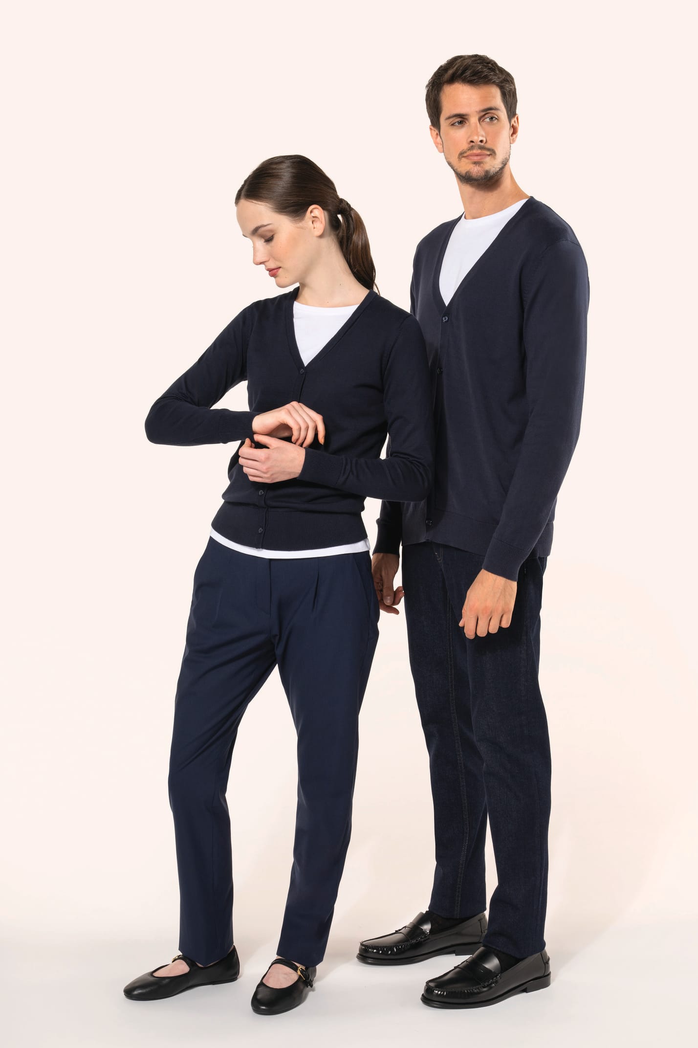 Jeune homme aux cheveux châtains courts et à la barbe naissante et jeune femme aux cheveux châtains longs attachés portent chacun un cardigan bleu profond en coton Supima®. Les fibres extra-longues de ce coton d’exception offrent souplesse, douceur et dur