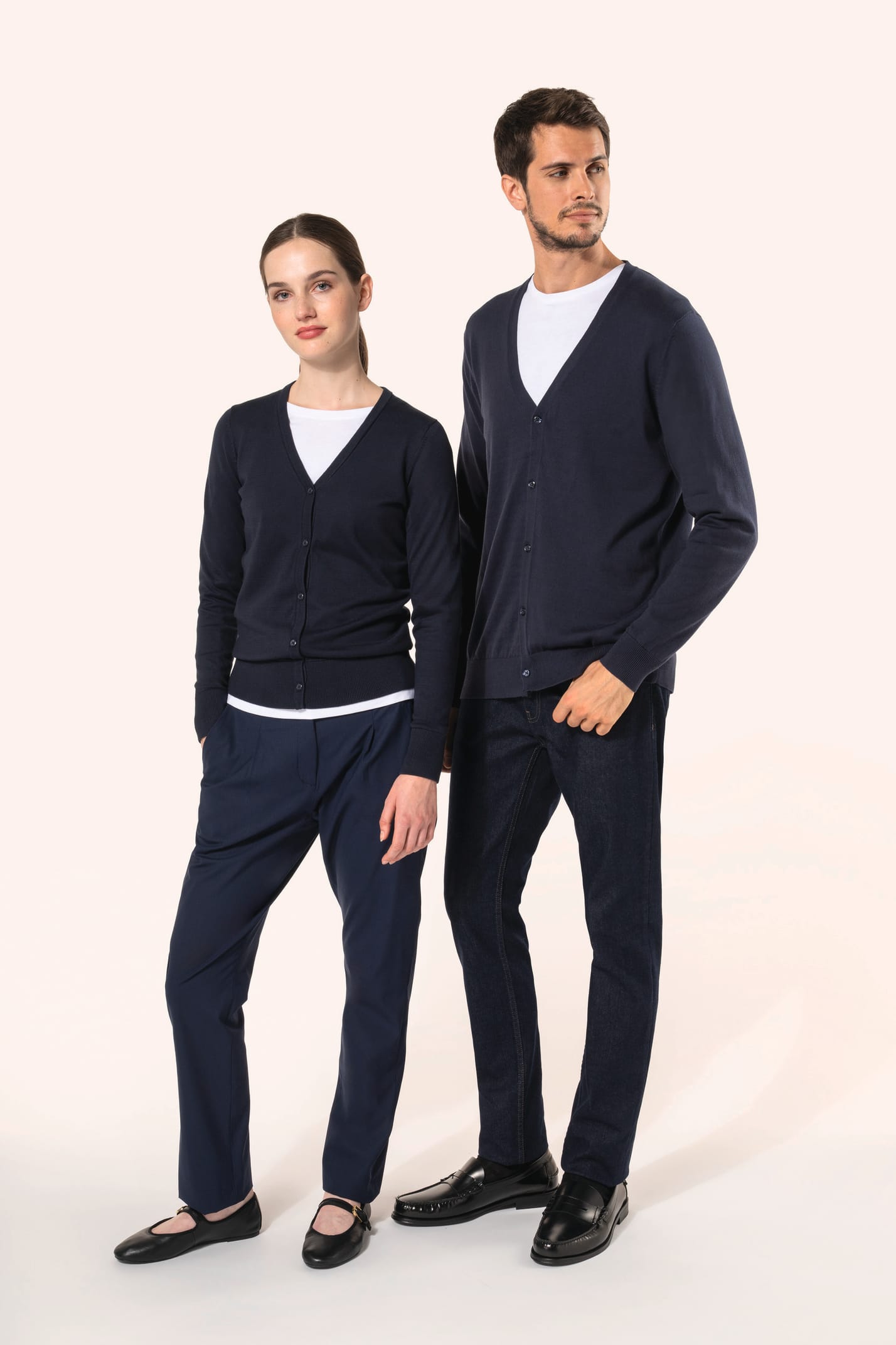 Jeune homme aux cheveux châtains courts et à la barbe naissante et jeune femme aux cheveux châtains longs attachés portent chacun un cardigan bleu profond en coton Supima®. Les fibres extra-longues de ce coton d’exception offrent souplesse, douceur et dur