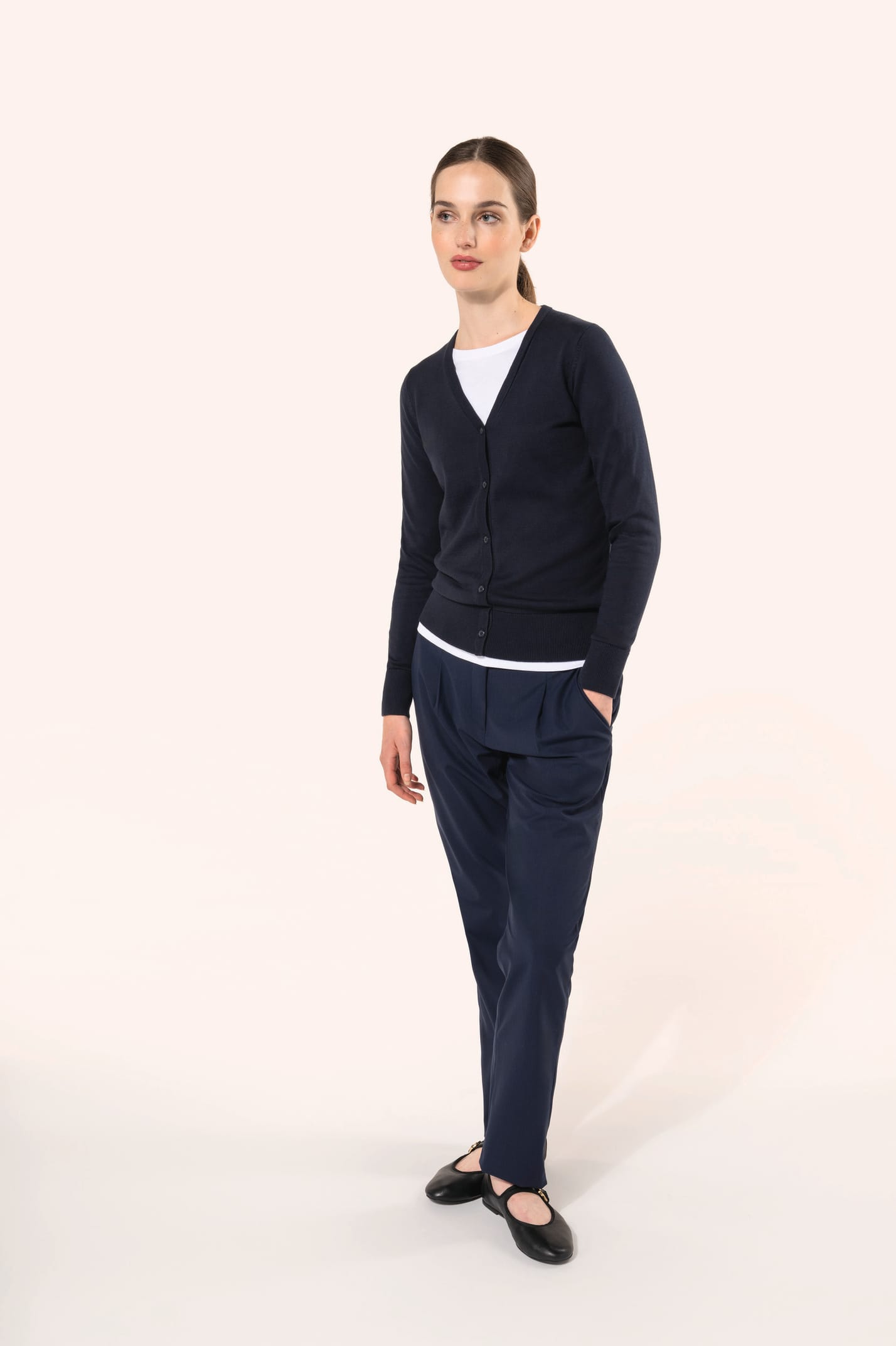 Jeune femme aux cheveux châtains longs attachés portant un cardigan bleu profond en coton Supima®. Ses fibres extra-longues apportent souplesse, douceur et durabilité à une maille de qualité supérieure. Confectionné en jauge 12 selon la technique fully-fa