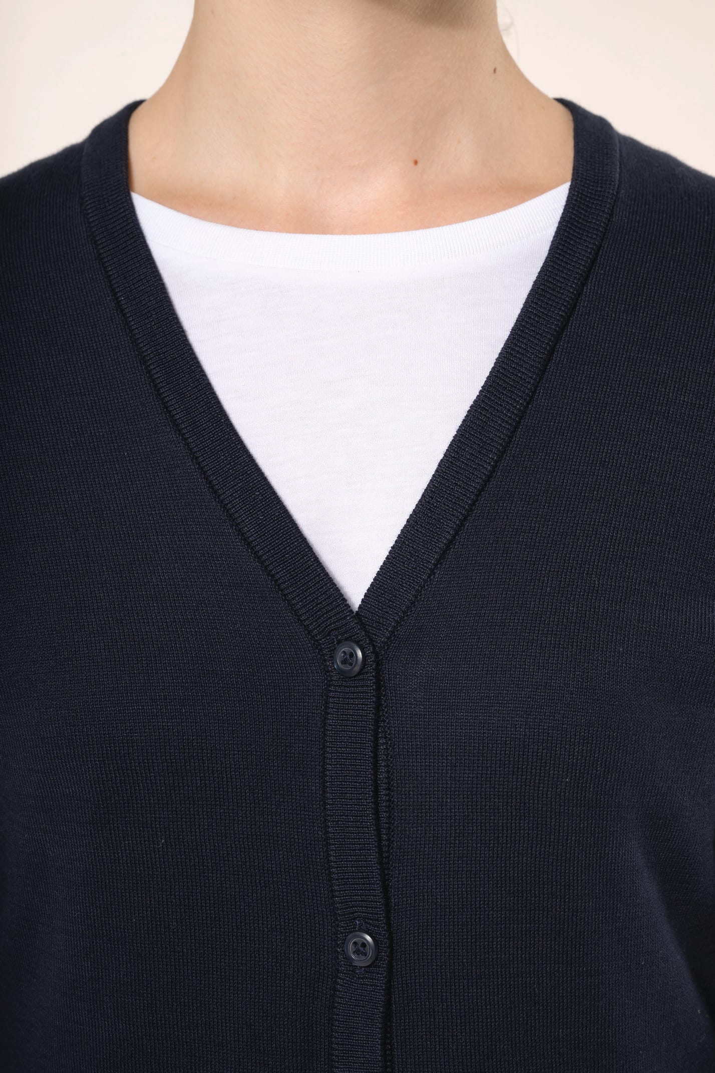 Jeune femme aux cheveux châtains longs attachés portant un cardigan bleu profond en coton Supima®. Ses fibres extra-longues apportent souplesse, douceur et durabilité à une maille de qualité supérieure. Confectionné en jauge 12 selon la technique fully-fa