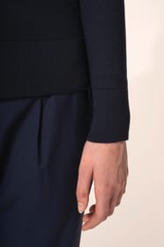 Jeune femme aux cheveux châtains longs attachés portant un cardigan bleu profond en coton Supima®. Ses fibres extra-longues apportent souplesse, douceur et durabilité à une maille de qualité supérieure. Confectionné en jauge 12 selon la technique fully-fa