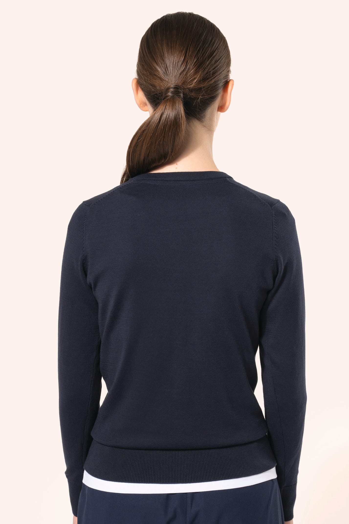 Jeune femme aux cheveux châtains longs attachés portant un cardigan bleu profond en coton Supima®. Ses fibres extra-longues apportent souplesse, douceur et durabilité à une maille de qualité supérieure. Confectionné en jauge 12 selon la technique fully-fa