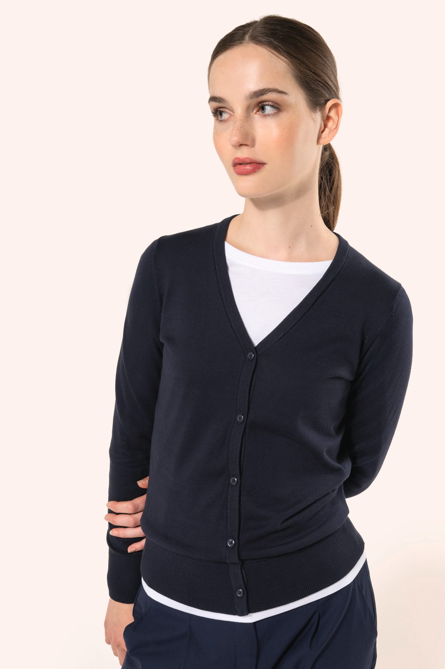 Jeune femme aux cheveux châtains longs attachés portant un cardigan bleu profond en coton Supima®. Ses fibres extra-longues apportent souplesse, douceur et durabilité à une maille de qualité supérieure. Confectionné en jauge 12 selon la technique fully-fa