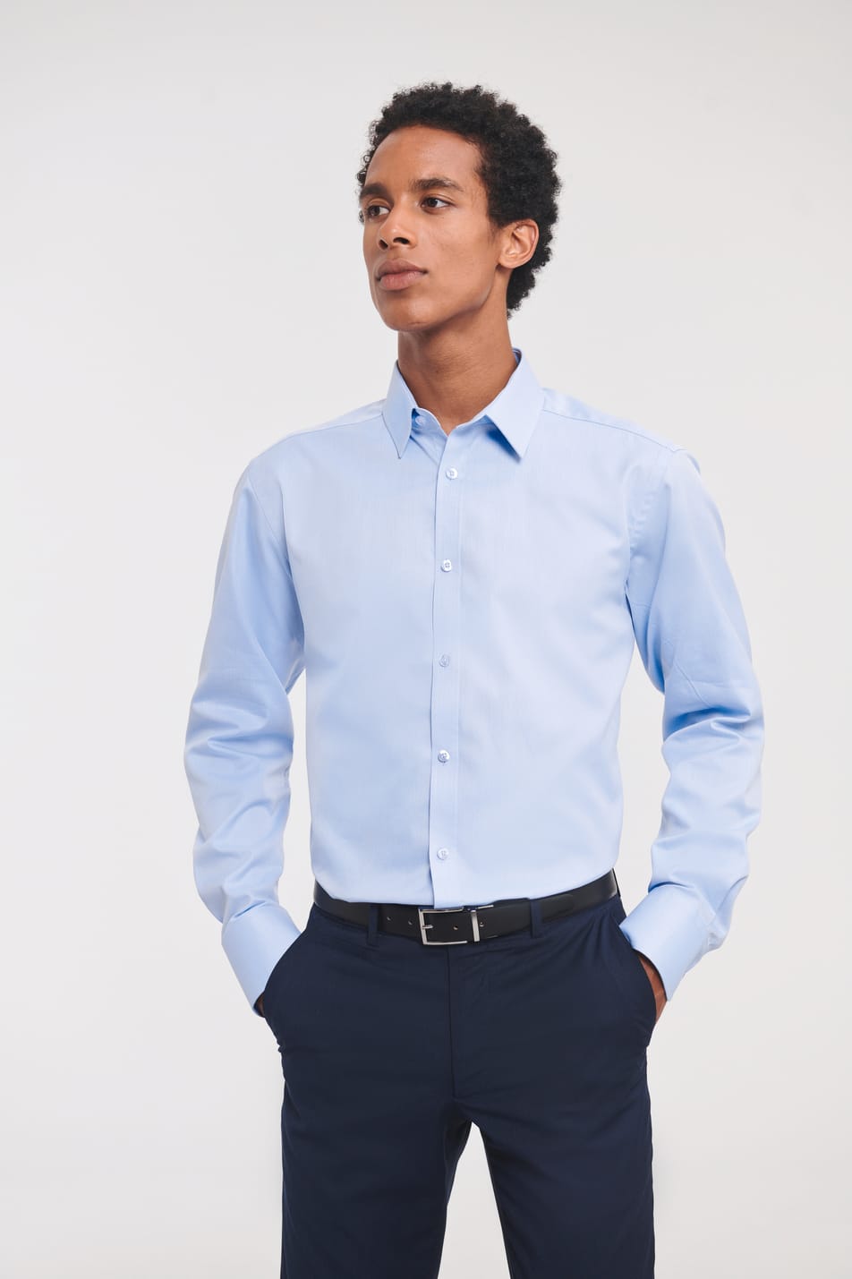 chemise bleu clair manches longues coupe ajustée col semi-évasé et patte de boutonnage étroite portée rentrée dans le pantalon par un homme avec les mains dans les poches