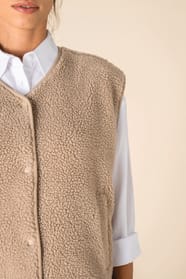 Détail du col d'un veste sans manches en sherpa beige portée par une femme