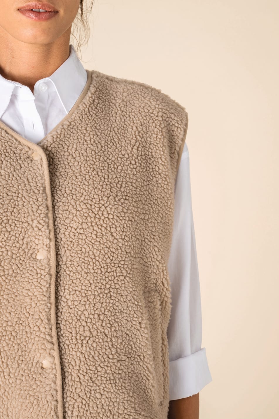 Détail du col d'un veste sans manches en sherpa beige portée par une femme