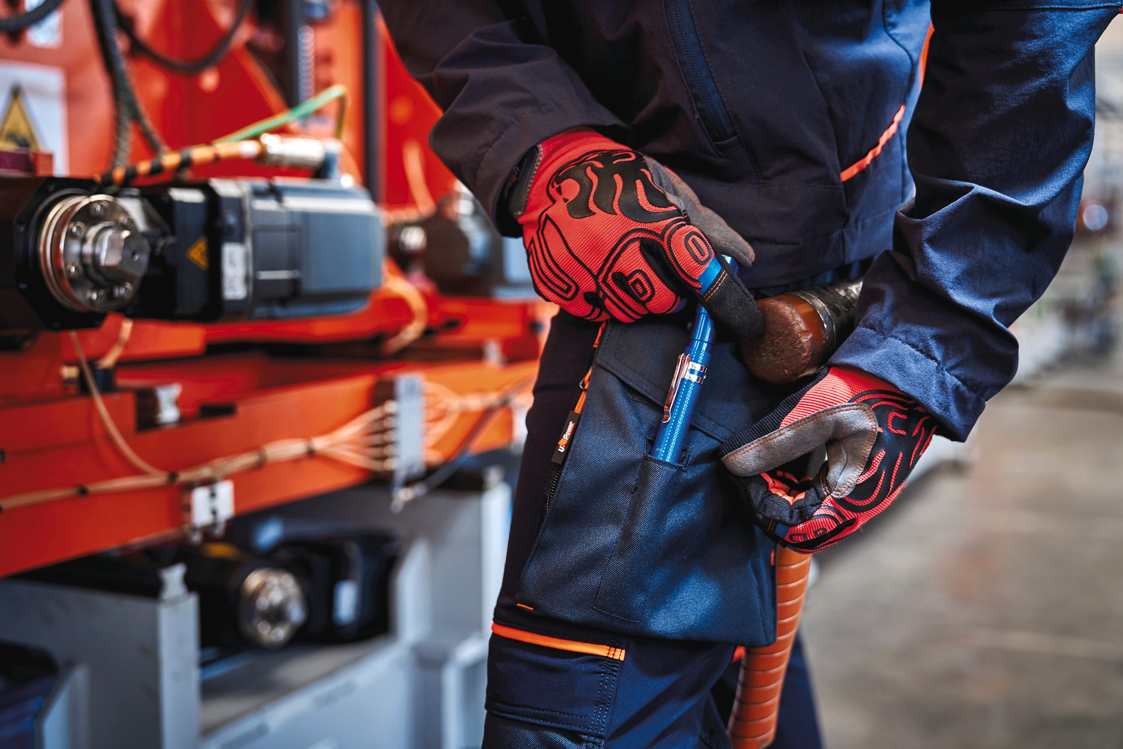 détail poche latérale sur pantalon bleu foncé avec détails oranges multipoches porté par un homme avec des gants et une veste assortie