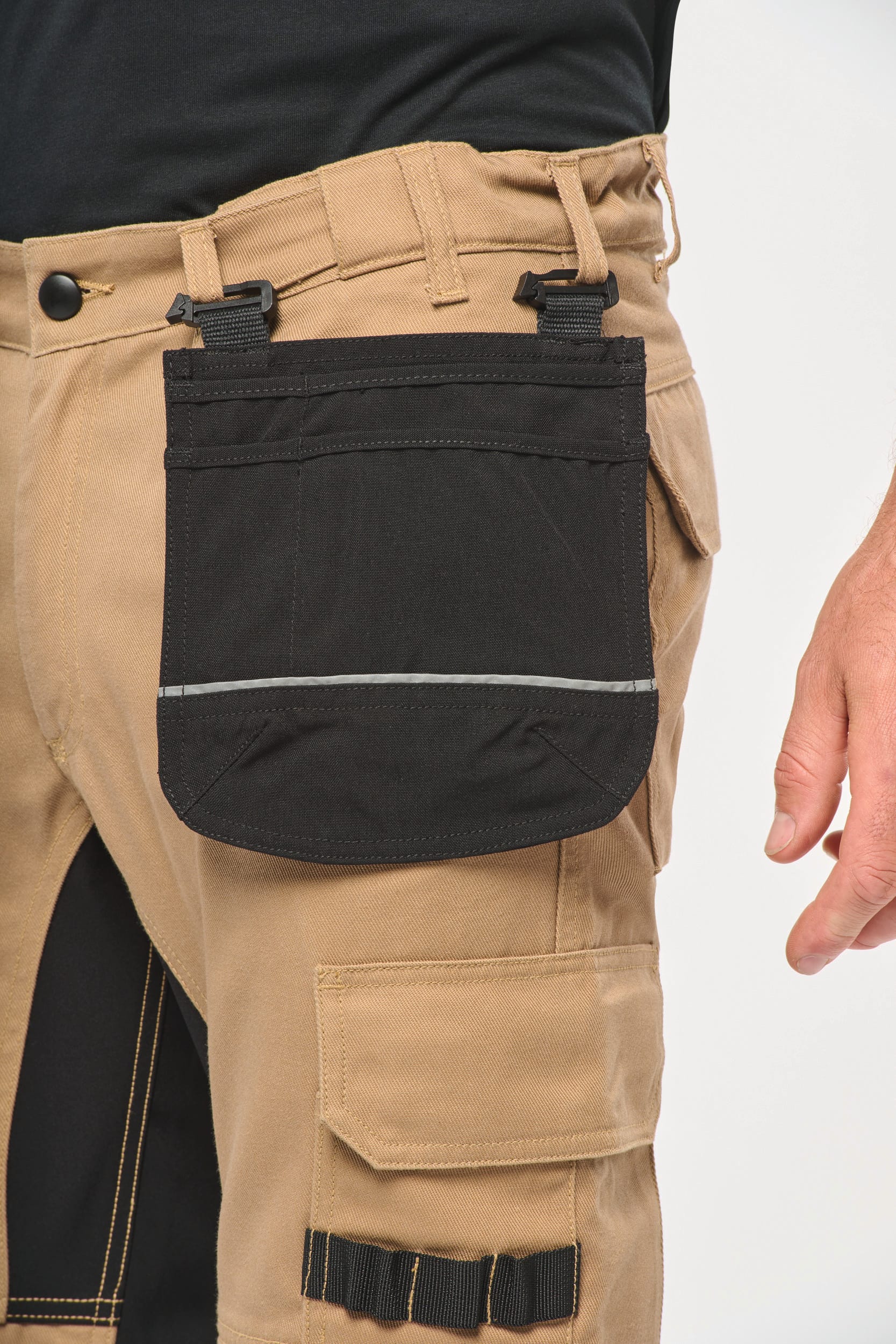 Poches à outils noire accrochées aux passants du pantalon.