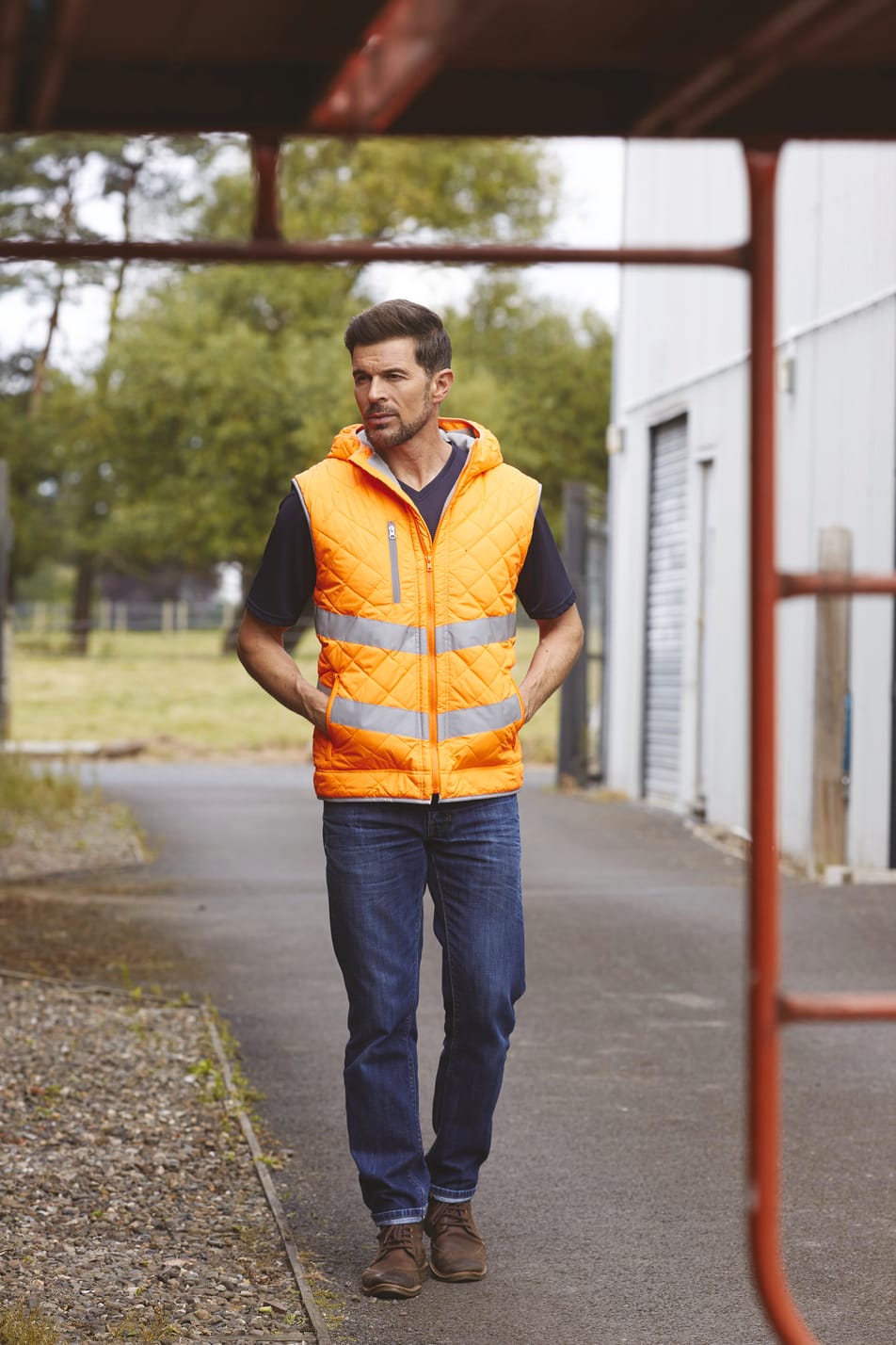 bodywarmer haute visibilité orange fluo avec bandes réfléchissantes et col montant multipoches porté par un homme qui marche