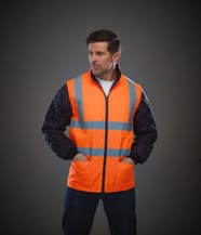gilet de sécurité sans manches orange fluo avec bandes réfléchissantes porté par un homme avec les pains dans les poches