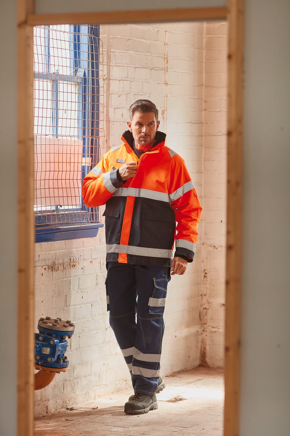 veste avec zip zippé bicolore orange fluo et bleu avec bandes réfléchissantes haute visibilité portée par un homme avec un pantalon bleu