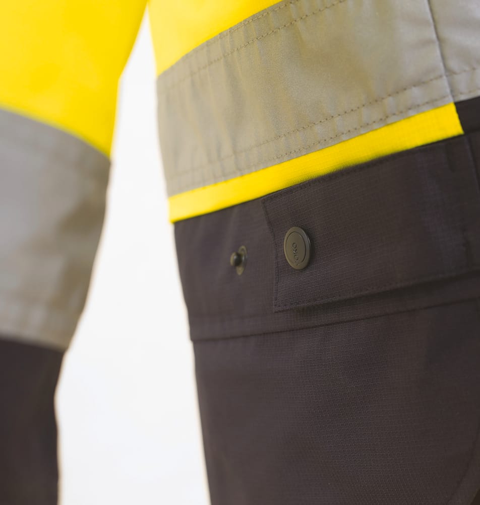 détail poche à bouton pression sur veste bicolore jaune fluo et bleu foncé haute visibilité avec bandes réfléchissantes