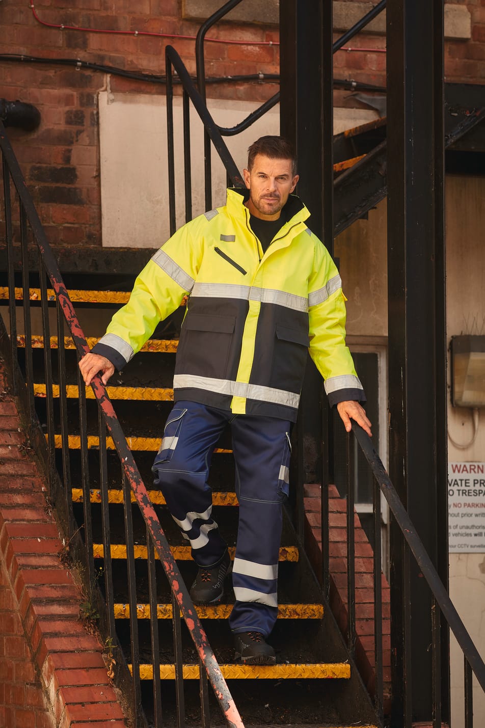 veste avec zip zippé bicolore jaune fluo et bleu avec bandes réfléchissantes haute visibilité portée par un homme avec un pantalon bleu