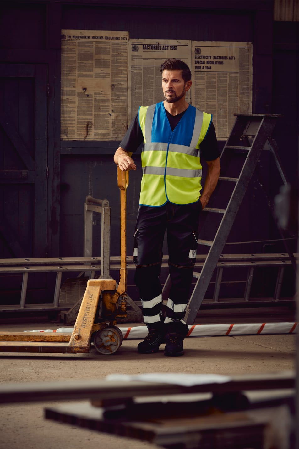 gilet bicolore bleu royal et jaune fluo haute visibilité avec bandes réfléchissantes sans manches fermeture velcro porté par un homme accoudé